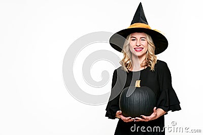Halloween Witch holding large black pumpkin winking. Beautiful young woman in witches hat and costume holding pumpkin. Stock Photo