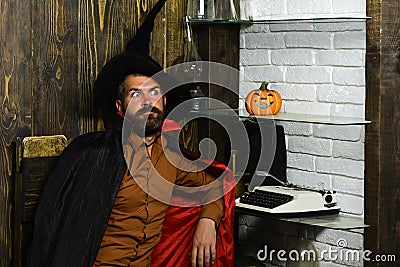 Halloween wizard sitting at pumpkin, typewriter, books on shelves Stock Photo