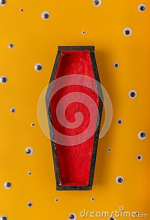 Halloween yellow background with an open red-black coffin in the center, around a scattering of plastic eyes of different sizes. A Stock Photo