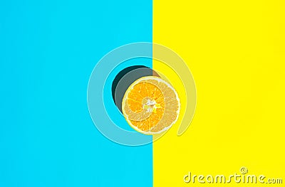 Halved Ripe Juicy Orange on Vivid Duotone Blue Yellow Background. Bright Harsh Sunlight Deep Shadow. Vibrant Neon Colors Stock Photo