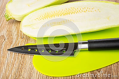 Halves of squash marrow and knife on plastic cutting board on table Stock Photo