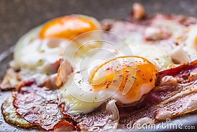 Ham and Eggs. Bacon and Eggs frying on ceramic pan. Salted egg and sprinkled with red pepper. English breakfast Stock Photo