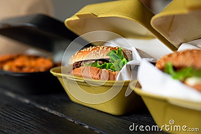 Hamburger in a takeaway container on the wooden background. Food delivery and fast food concept Stock Photo