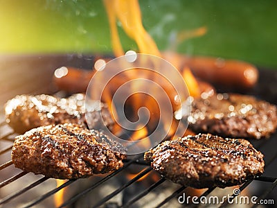 Hamburgers and hotdogs cooking on flaming grill Stock Photo