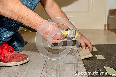 Hammer handle held by the hand with two amputated fingers of a person with dirty slippers as he works laying floors in his house. Stock Photo