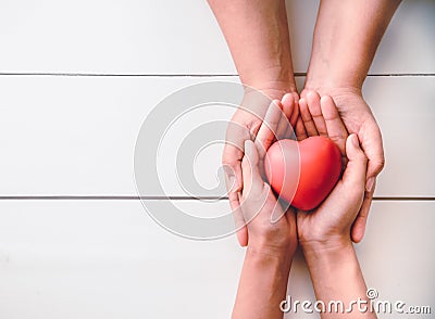 The hand of an adult holding a child`s hand with a red heart in Stock Photo