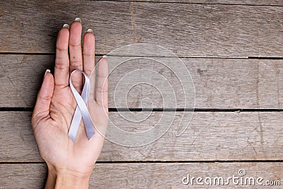 Hand of african american mid adult woman holding white lung cancer awareness ribbon wooden table Stock Photo