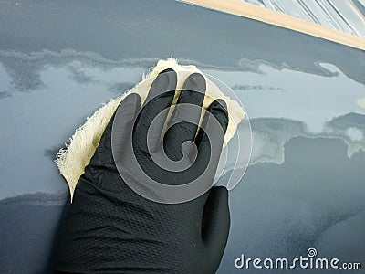 the hand of the auto painter in a black glove holds a special napkin for dusting the surface of the car. Stock Photo