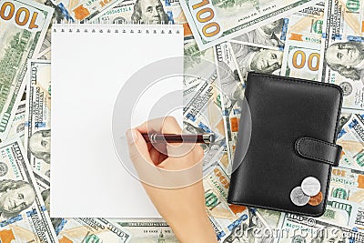 Hand with ballpoint pen over blank notebook on background of dollar bills and coins on wallet Stock Photo