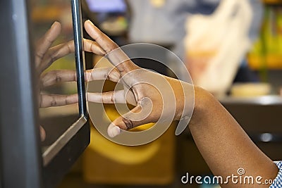 Hand of black girl cashier using touch screen cash register with blurred bokeh background - reflection of hand in screen Stock Photo