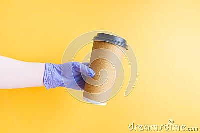 hand in a blue disposable rubber glove holds a shiny gold disposable cardboard cup of coffee for fast food Stock Photo