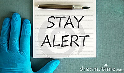 Hand in blue glove, pen, white note with words `stay alert Stock Photo