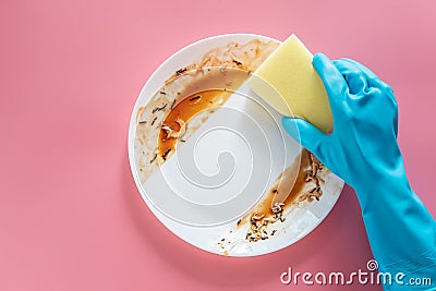 Hand in blue rubber glove hold yellow cleaning sponge to clean up and washing food stains and dirt on white dish after eating meal Stock Photo