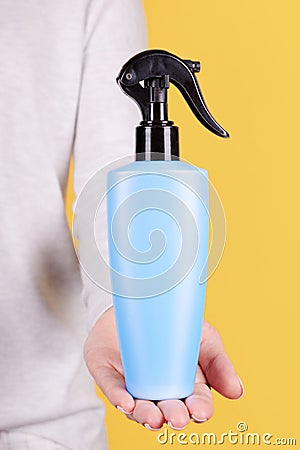 Hand with blue sun protection spray bottle. Isolated on yellow background Stock Photo