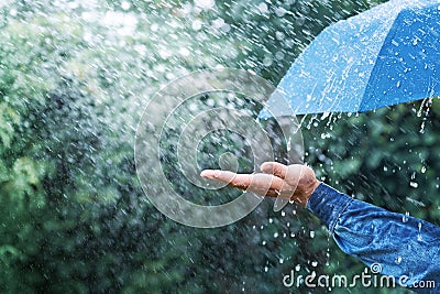 Hand and blue umbrella under heavy rain against nature background. Rainy weather concept Stock Photo