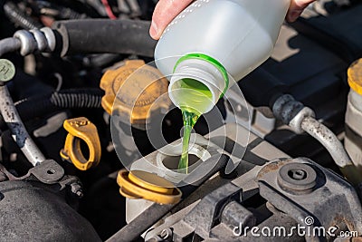 Hand with bottle pouring antifreeze coolant into the expansion tank. Dusty details of a flat-four boxer car engine compartment Stock Photo