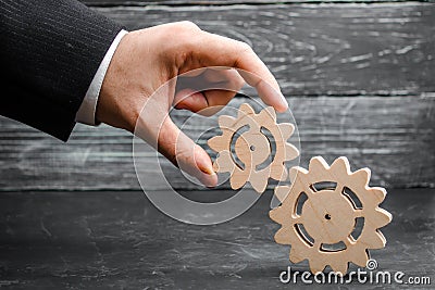 The hand of a businessman adds a gear to a large gear. The concept of business management, the search for compromise Stock Photo