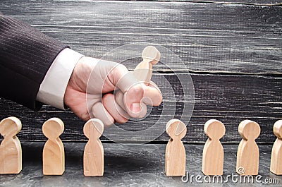 The hand of a businessman grabs a wooden figure of a man from a number of workers. The concept of business management Stock Photo