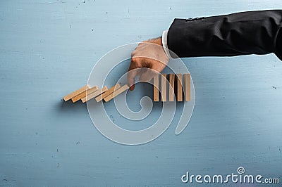 Hand of a businessman stopping collapsing dominos in a conceptual image of crisis management Stock Photo