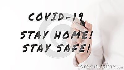 Hand of a businessman writing covid-19, stay home, stay safe message with marker in a conceptual image of coronavirus Stock Photo