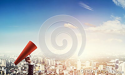 Hand of businesswoman holding red paper trumpet against cityscape background Stock Photo