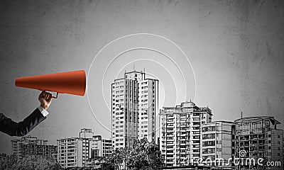 Hand of businesswoman holding red paper trumpet against cityscape background Stock Photo