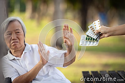 Hand of caregiver giving medicine pills and capsules to the elderly,asian senior woman refusing to take medication,afraid,bad side Stock Photo