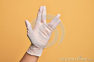 Hand of caucasian young man with medical glove over isolated yellow background greeting doing Vulcan salute, showing hand palm and Stock Photo