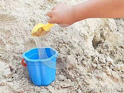 Hand of child playing in the sandbox with yellow scoop and blue bucket Stock Photo