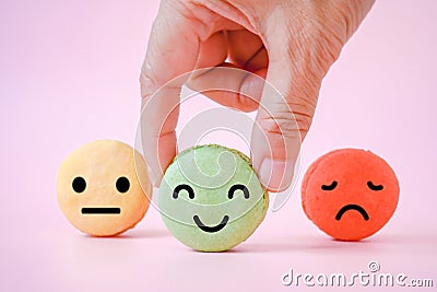 Hand choose happy face icon on green macaron with blurred others on sweet pink background Stock Photo