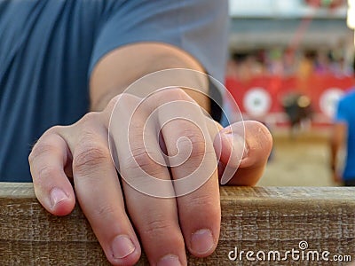 hand clinging to the wooden trench with bull in the background blurred of bulls Stock Photo