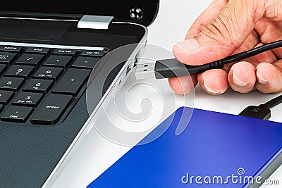 Hand connecting external hard drive usb cable to laptop on white desk Stock Photo