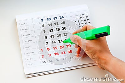 Hand crosses off the green marker days in the calendar. White calendar. Weekends are highlighted in red. Close up Stock Photo