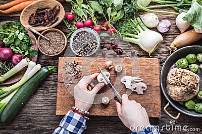 Hand cutting vegetables.Women hands is slicing mushrooms on wooden board near vegetables. Stock Photo