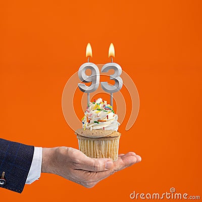 The hand that delivers cupcake with the number 93 candle - Birthday on orange background Stock Photo