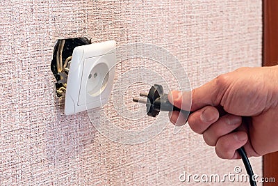Hand disconnects or connects the plug to a broken outlet, risk of electric shock Stock Photo