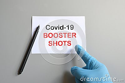 The hand of the doctor with the blue glove writes on white paper the text `Covid-19 Booster Shoots`. Concept of Combating the Stock Photo