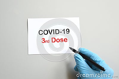 The hand of the doctor with the blue glove writes on white paper the text `Covid-19 3rd Dose`. Concept of Combating the COVID-19 Stock Photo