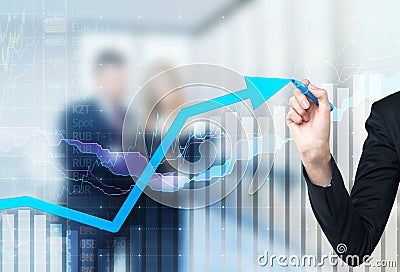 A hand is drawing a growing arrow on the glass scree, Blue dark background with financial graphs. Stock Photo