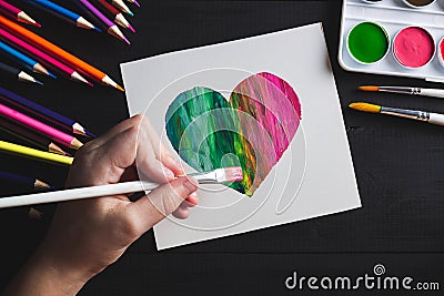 Hand drawing multi-colored heart with paints and pencils lying on black wooden table. Flat lay Stock Photo