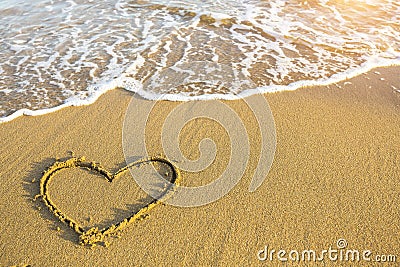 Hand drawn heart on beach sand over soft gold sunset. Love. Stock Photo