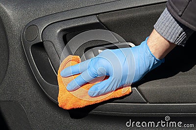 Hand of driver in blue protective glove is wiping with a cloth an interior handle of car door. Coronavirus or Covid-19 car Stock Photo