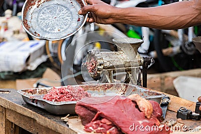 Hand driving away flies over minced meat next to a grinder outdoors in Toliara Stock Photo