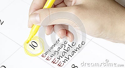 Hand encircles a date on a calendar with text Empower Engage Enable Enhance yellow felt-tip pen Stock Photo
