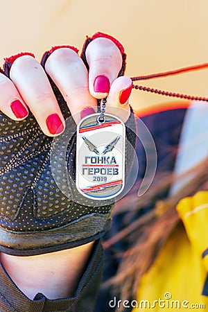 The hand of a female athlete shows the medal received in the race of heroes. Text in Russian: Race of Heroes Editorial Stock Photo