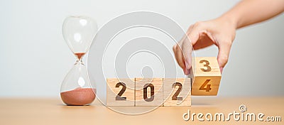 hand flipping block 2023 to 2024 text with hourglass on table. Resolution, time, plan, goal, motivation, reboot, countdown and Stock Photo