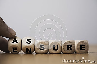 Hand flipping wooden cube block for change between Assure and Ensure for Insurance and assurance concept Stock Photo