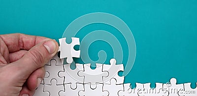 The hand folds a white jigsaw puzzle against the background of the blue surface. Texture photo with space for text Stock Photo