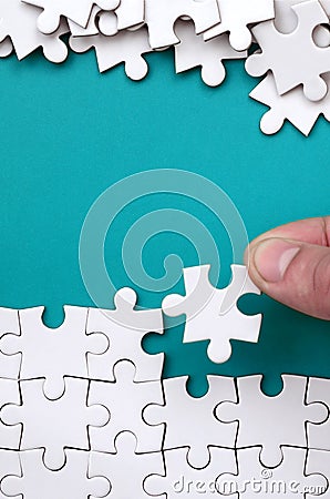 The hand folds a white jigsaw puzzle and a pile of uncombed puzzle pieces lies against the background of the blue surface. Texture Stock Photo