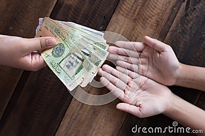 Hand giving Saudi Riyal bank notes Stock Photo